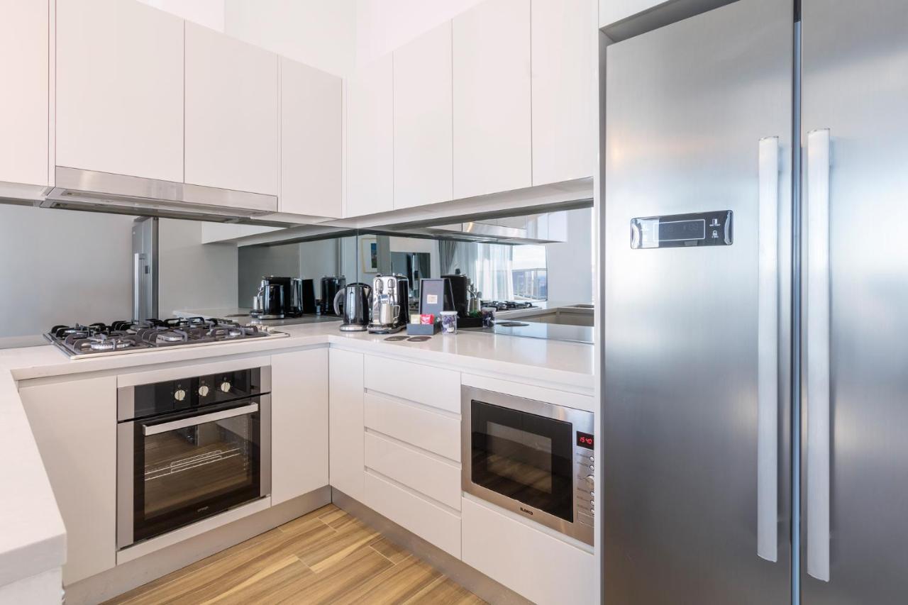 Meriton Suites Bondi Junction Sydney Exterior foto The photo shows a modern kitchen with a clean and minimalist design. It features white cabinetry and a stainless steel refrigerator. The kitchen includes a gas stove with an oven below it, as well as a microwave. There are several kitchen appliances,