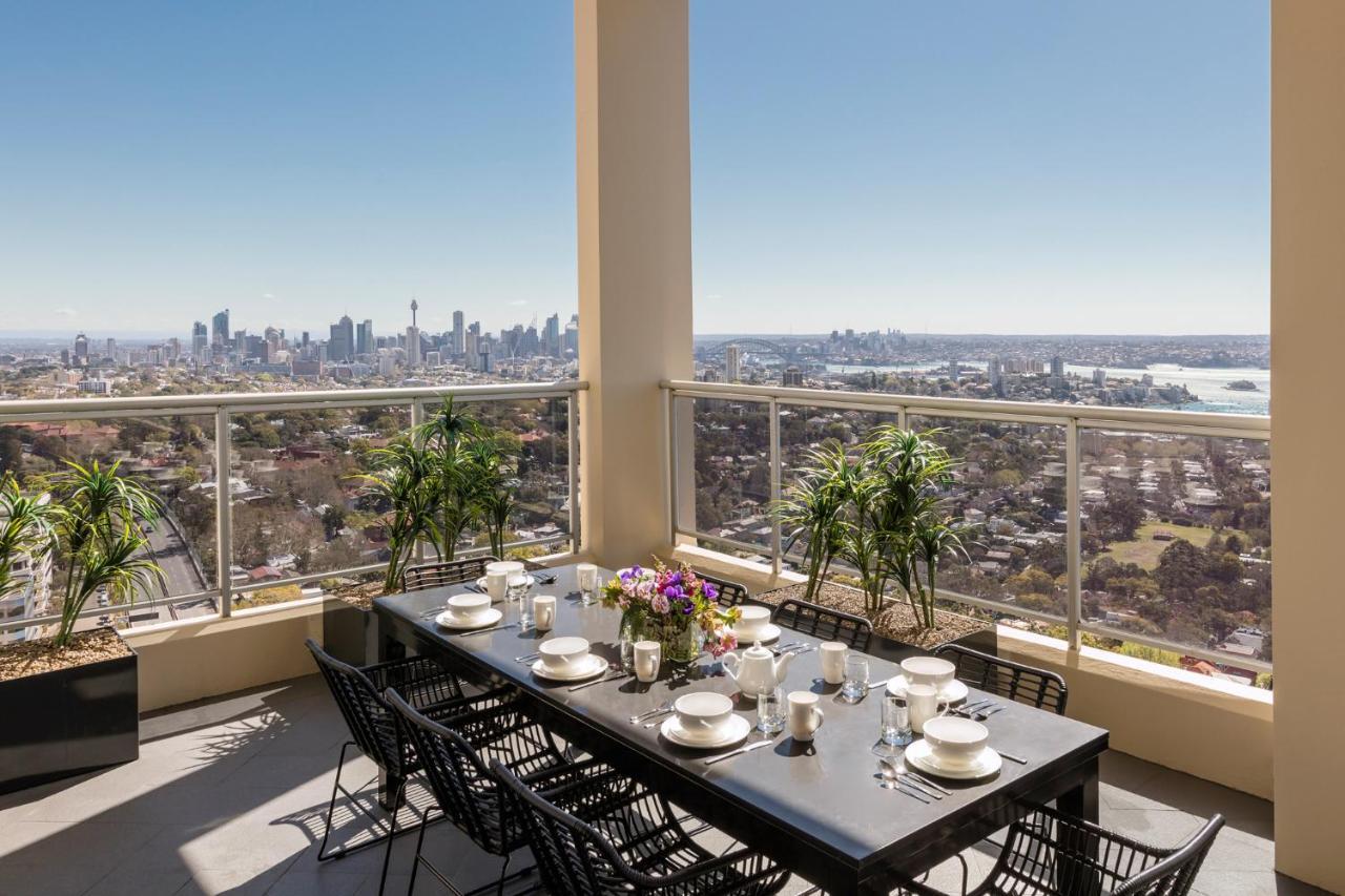 Meriton Suites Bondi Junction Sydney Exterior foto The photo shows a beautifully arranged outdoor dining area on a balcony. There is a long black dining table set for a meal, with plates, glasses, and decorative items like a vase of flowers. Surrounding the table are stylish black chairs. In the back