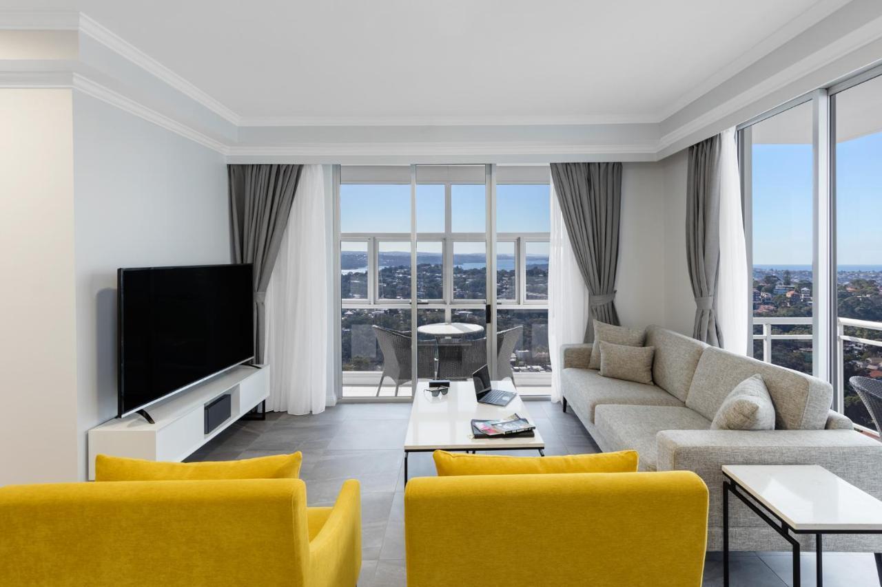 Meriton Suites Bondi Junction Sydney Exterior foto The photo depicts a modern living room space with large windows that offer a view of the outside. The decor is minimalist and stylish, featuring a light color palette. 

In the center, there are two bright yellow chairs facing each other. A sleek, re