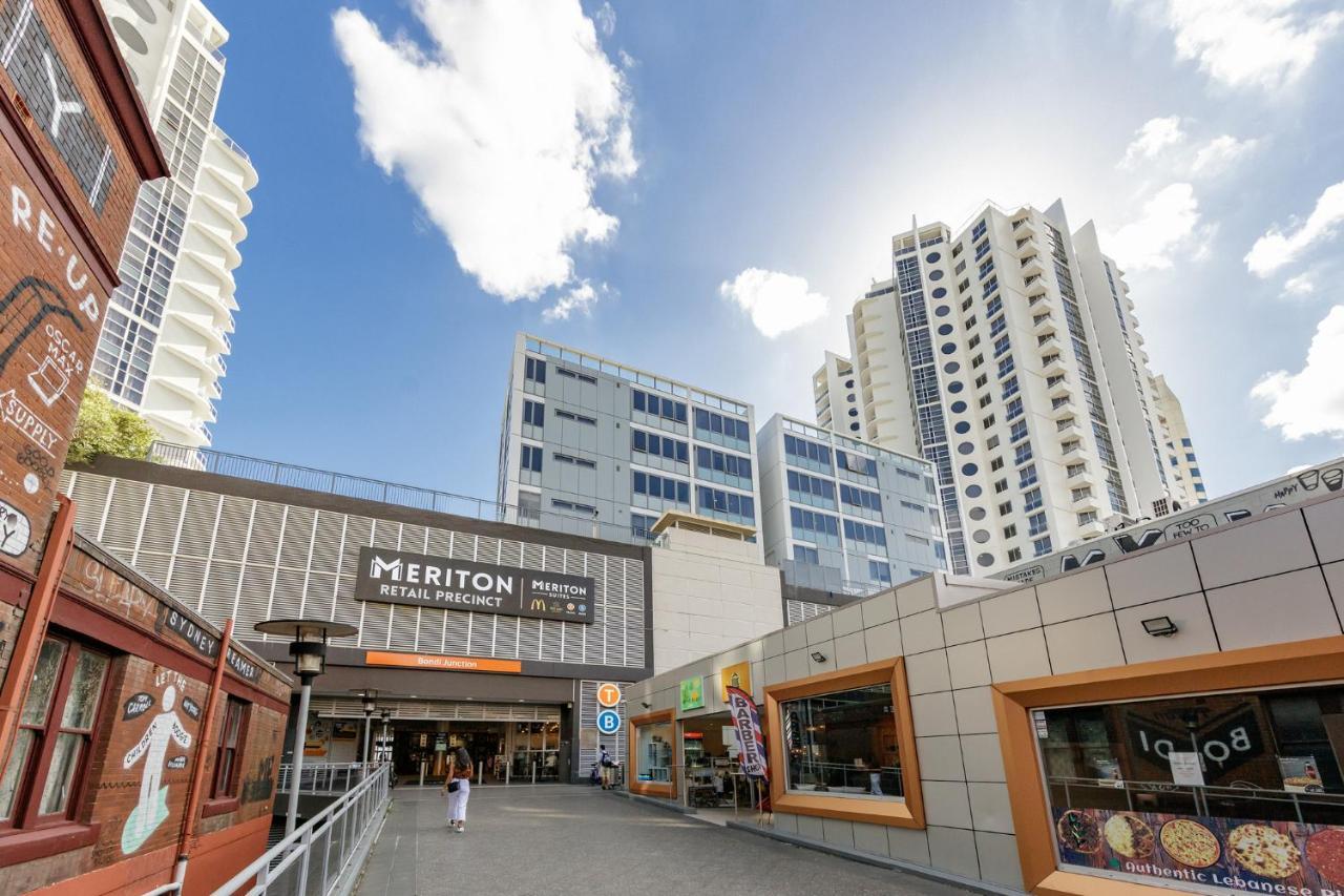 Meriton Suites Bondi Junction Sydney Exterior foto The photo depicts a modern urban environment featuring a building labeled "Meriton Retail Precinct." In the foreground, there are shops with colorful signage, while in the background, tall residential buildings tower over the area. The sky above is b