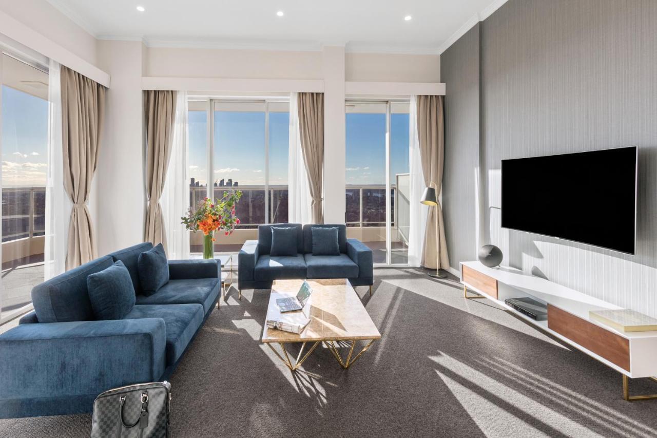 Meriton Suites Bondi Junction Sydney Exterior foto The photo depicts a modern living room with a stylish and contemporary design. It features a cozy seating arrangement with a blue sofa and two matching armchairs. In front of the seating area is a coffee table with a geometric design. The room has la