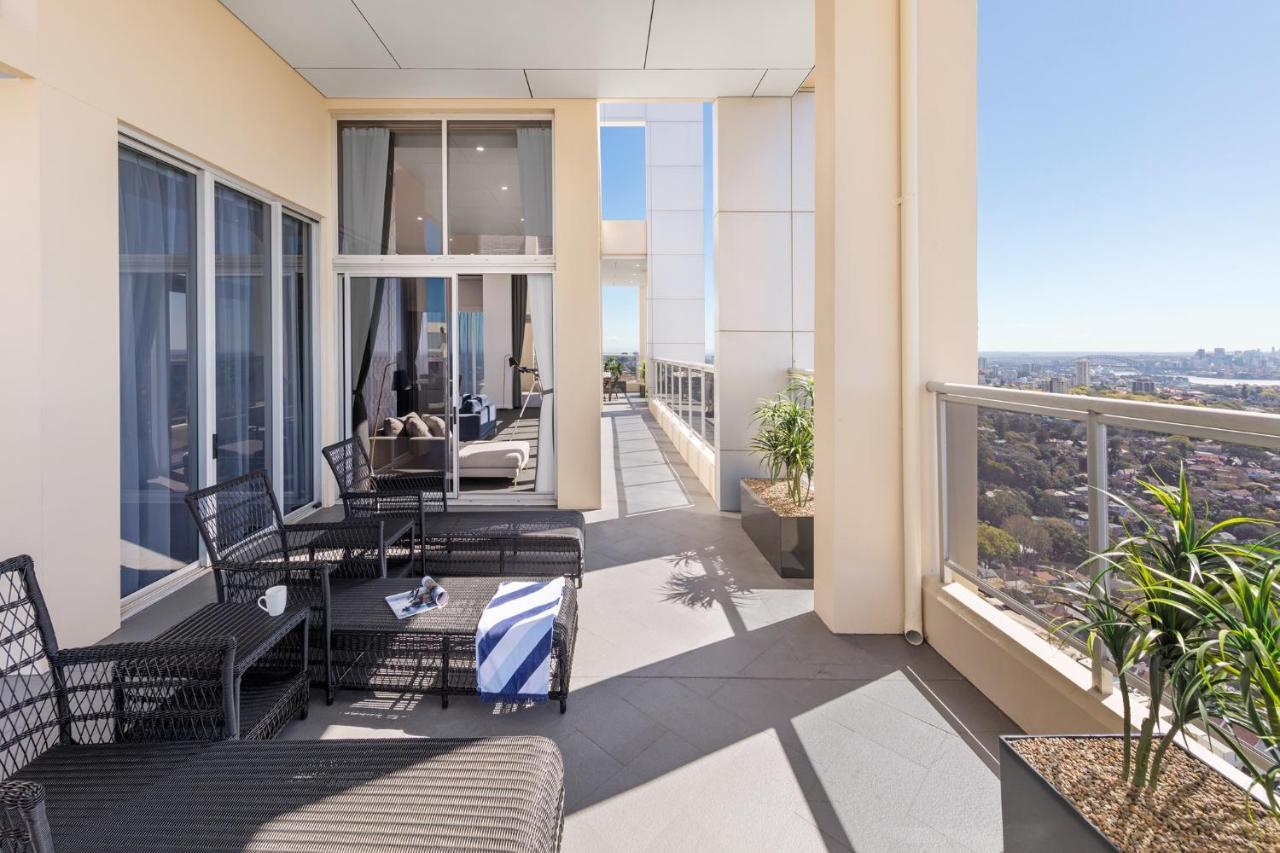 Meriton Suites Bondi Junction Sydney Exterior foto The photo shows a spacious balcony or terrace area of a high-rise building. It features modern outdoor furniture, including a seating arrangement with dark wicker chairs and a table. There are cushions, and a blue and white striped blanket is draped 