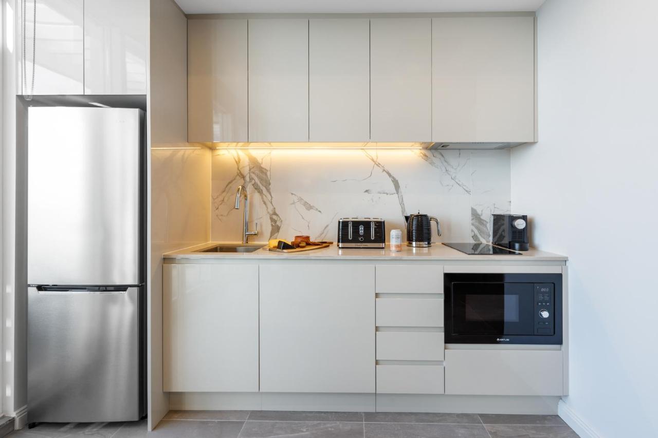 Meriton Suites Bondi Junction Sydney Exterior foto The photo shows a modern kitchen featuring a sleek design. It includes light-colored cabinetry with a smooth finish and upper cabinets that blend seamlessly with the wall. The countertop is made of a light stone, complementing the overall aesthetic. 