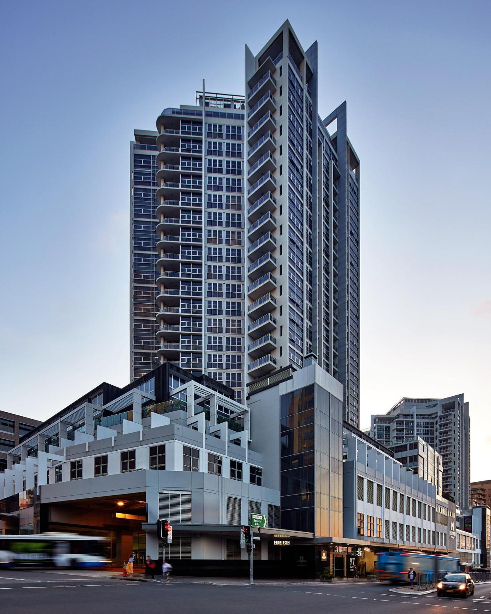 Meriton Suites Bondi Junction Sydney Exterior foto The image shows a modern high-rise building with a sleek design. The structure features a mix of glass and concrete elements, with multiple levels showcasing balconies. The building appears to be part of an urban environment, likely containing reside