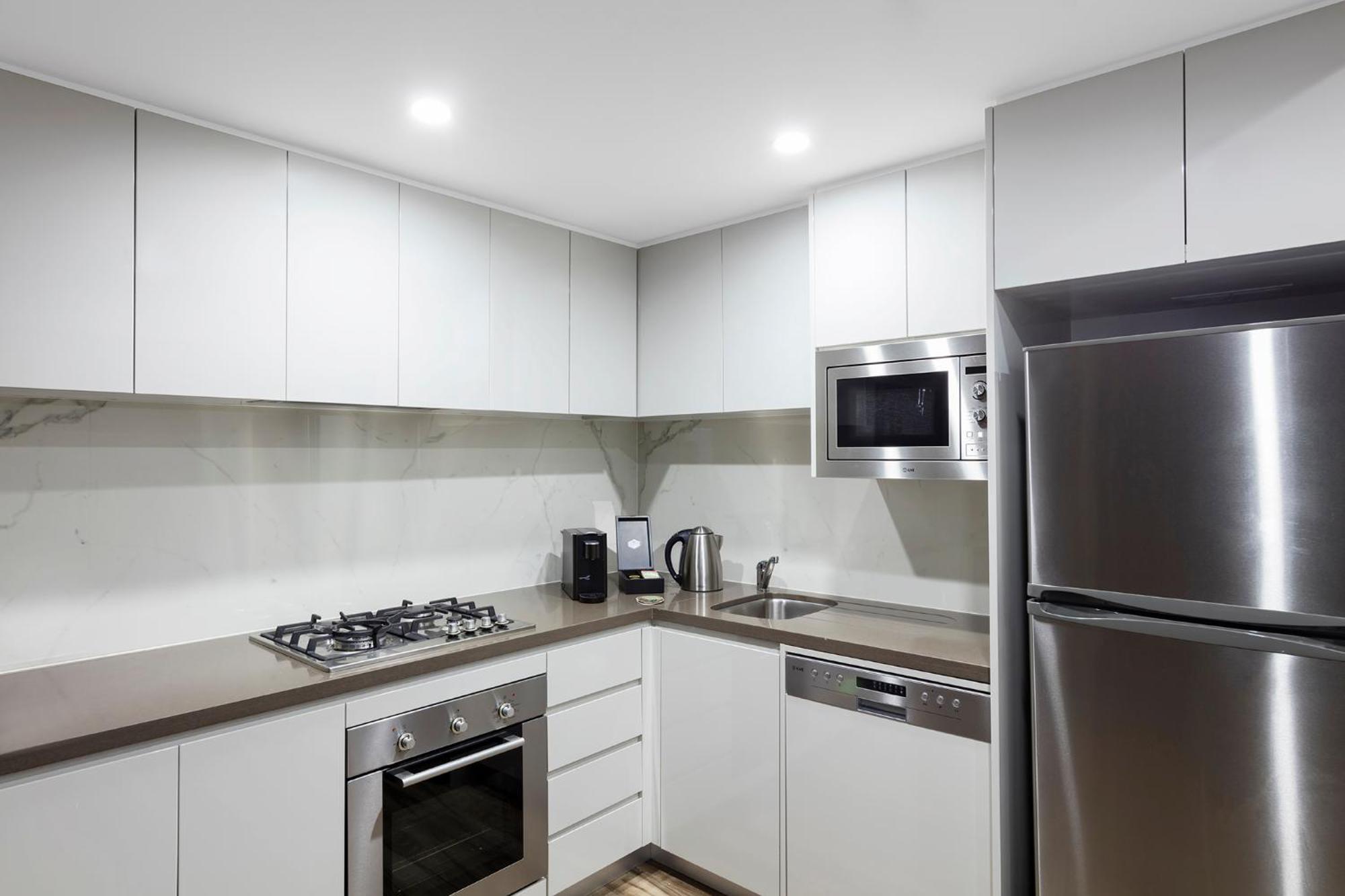 Meriton Suites Bondi Junction Sydney Exterior foto The photo shows a modern kitchen featuring a minimalist design. It has light-colored cabinetry, a countertop, and stainless steel appliances. The appliances include a gas stove with multiple burners, an oven, a microwave, a kettle, and a refrigerator