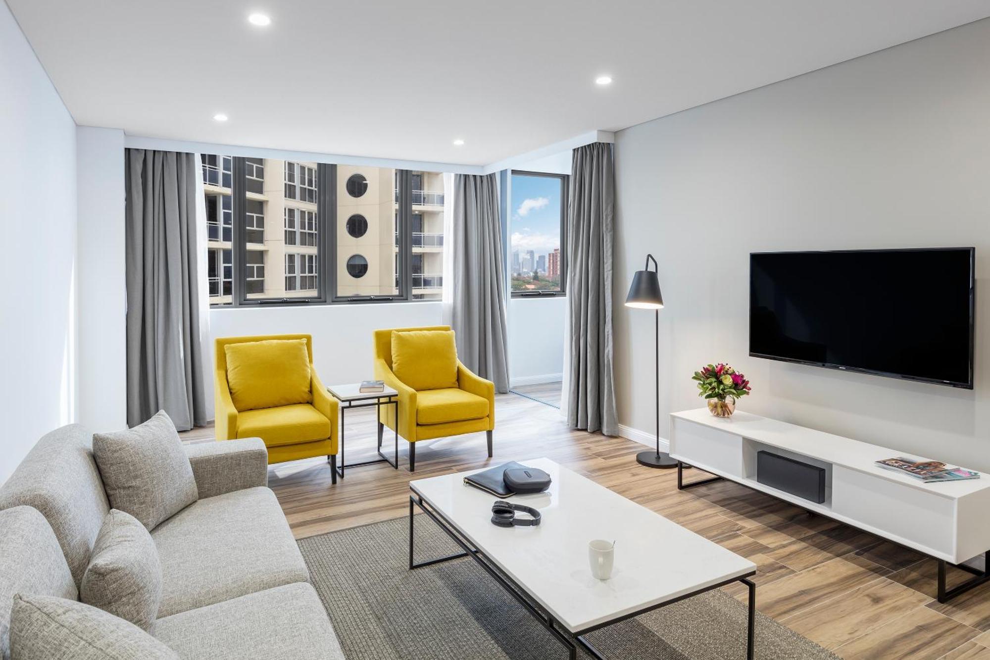 Meriton Suites Bondi Junction Sydney Exterior foto The photo shows a modern, well-lit living room. It features a light gray sofa with a textured fabric. There are two bright yellow armchairs positioned near a window, which allows natural light to enter the space. The room has light gray curtains and 